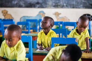 actionaid.gr παιδιά στην στην τάξη με κίτρινα πουκάμισα και μπλε καρέκλες | YouBeHero