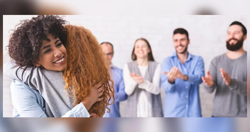  δυο γυναίκες που είναι αγκαλιά και στο φόντο άνθρωποι να χειροκροτούν