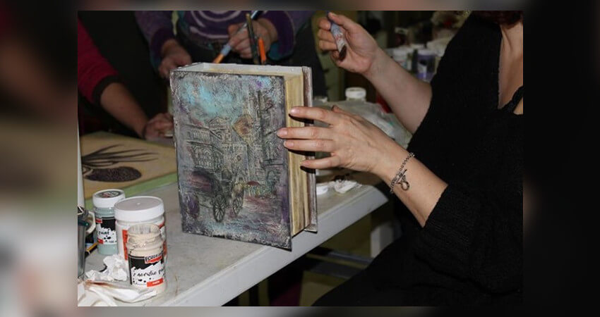 Μια γυναίκα που κατασκευάζει ένα βιβλίο με κάποια μορφή τέχνης σε ένα τραπέζι με υλικά χειροτεχνίας