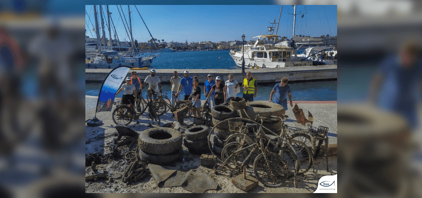 11 άτομα σε ένα λιμάνι μπροστά από χρησιμοποιημένα λάστιχα φορτηγών και σκουριασμένα ποδήλατα, τα οποία έχουν ανασυρθεί από την θάλασσα